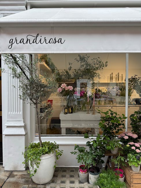 View of a florist shop named 'grandirosa' with a large glass window showcasing an interior decorated with fresh pink and white flowers, including hydrangeas and roses, arranged in vases and bouquets. 